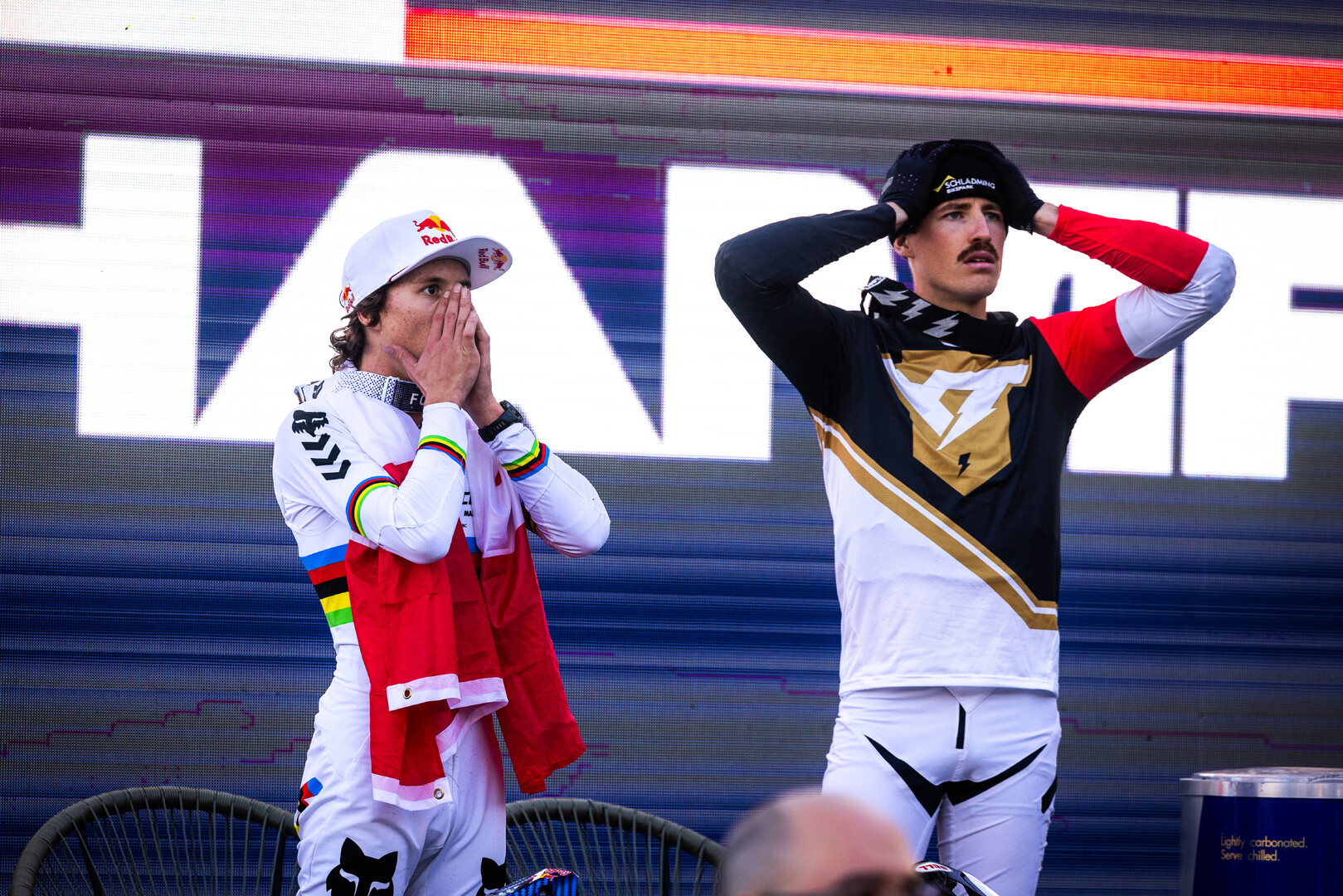 Due rider reagiscono con tensione davanti al tabellone di una gara downhill